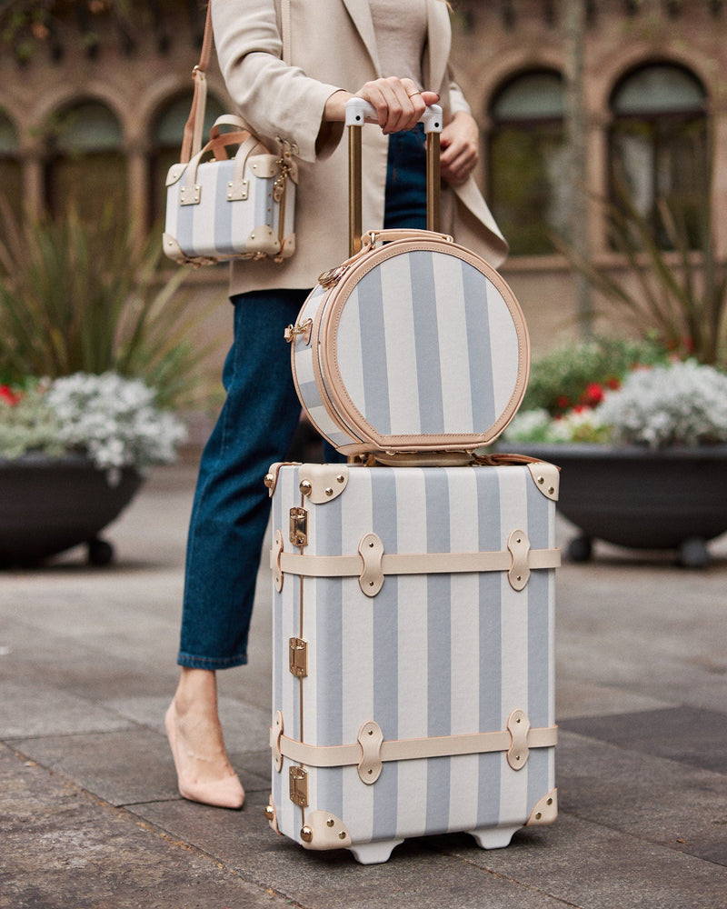 Lifestyle image of model with The Illustrator fibreboard suitcases in blue-stripe
